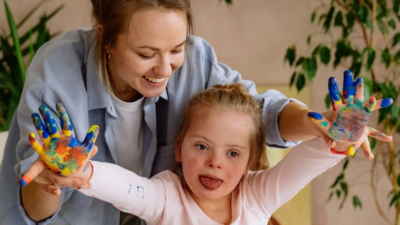 Une accompagnante et une petite fille montrent leurs mains pleines de peinture